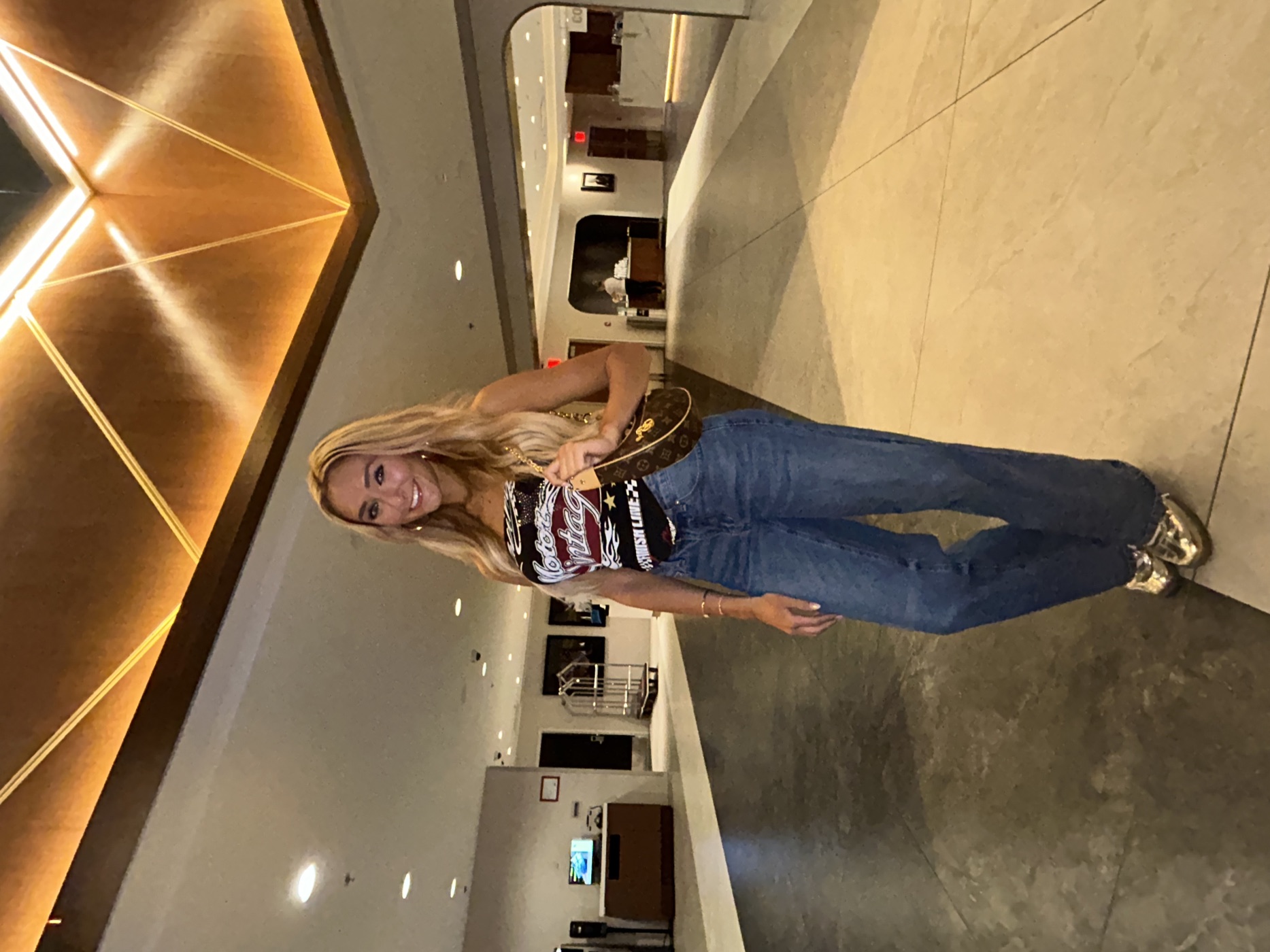 Racing graphic tube top, mid-wash baggy jeans and gold Samba OG sneakers in a hotel lobby.