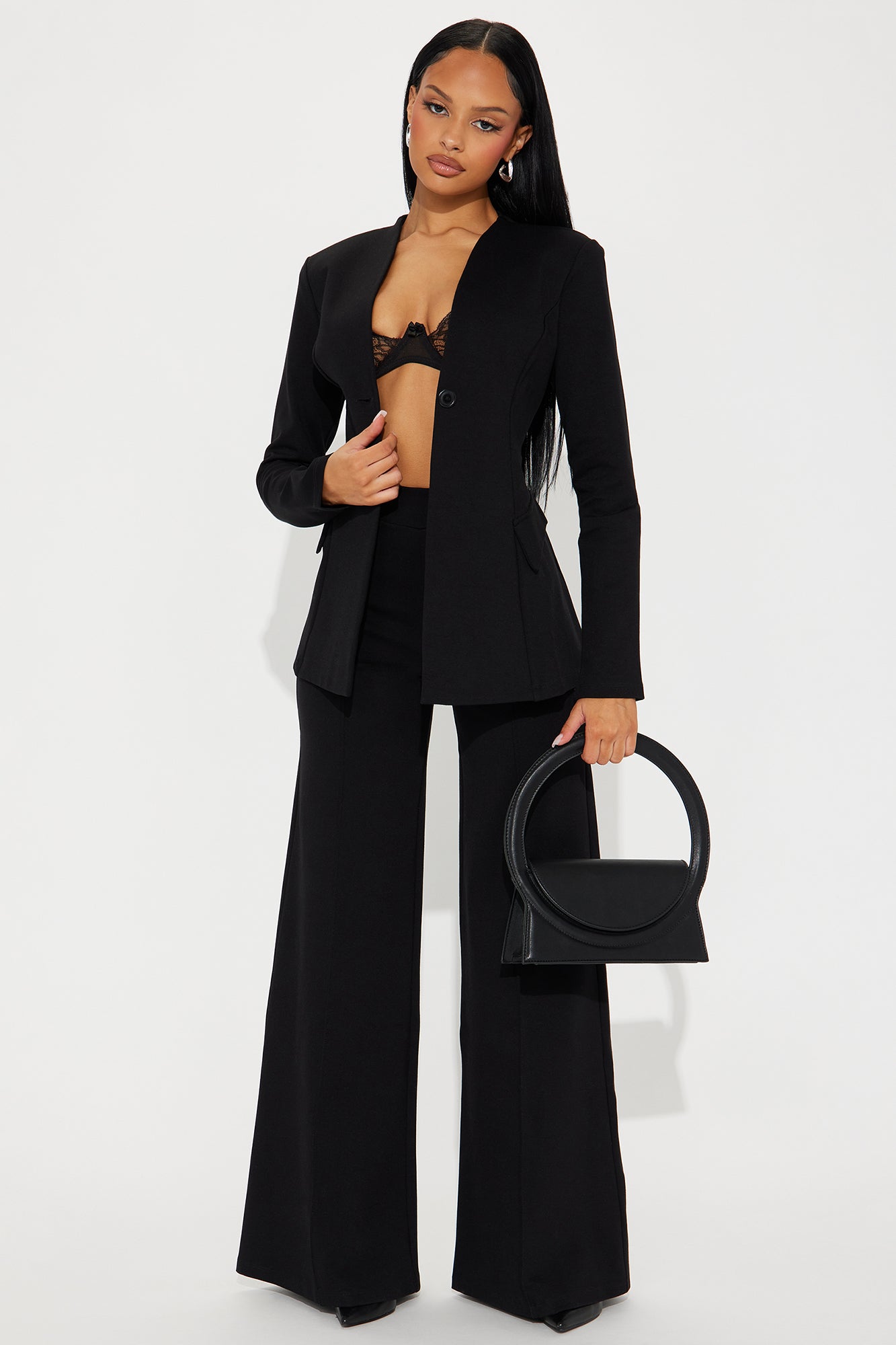 A model in a tailored black blazer and wide-leg trousers, holding a structured black handbag.